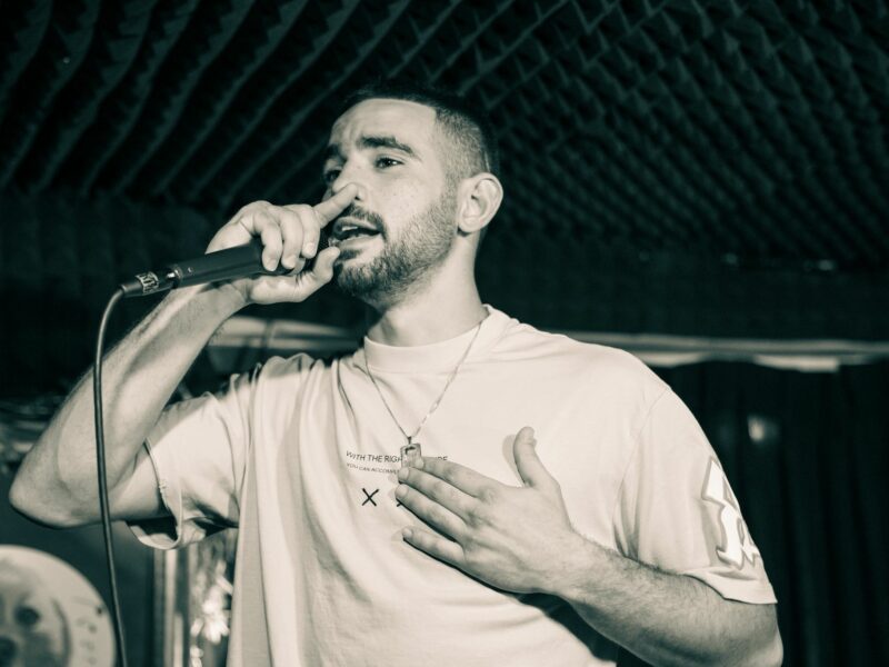 תמונה בשחור-לבן של גבר מחזיק מיקרופון ושר באולפן, משויט יד על הלב