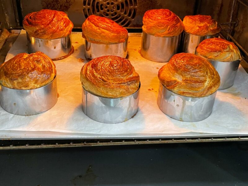 "מאפים עגולים תפוחים נאפים בתנור בתוך טבעות מתכת על נייר אפייה."