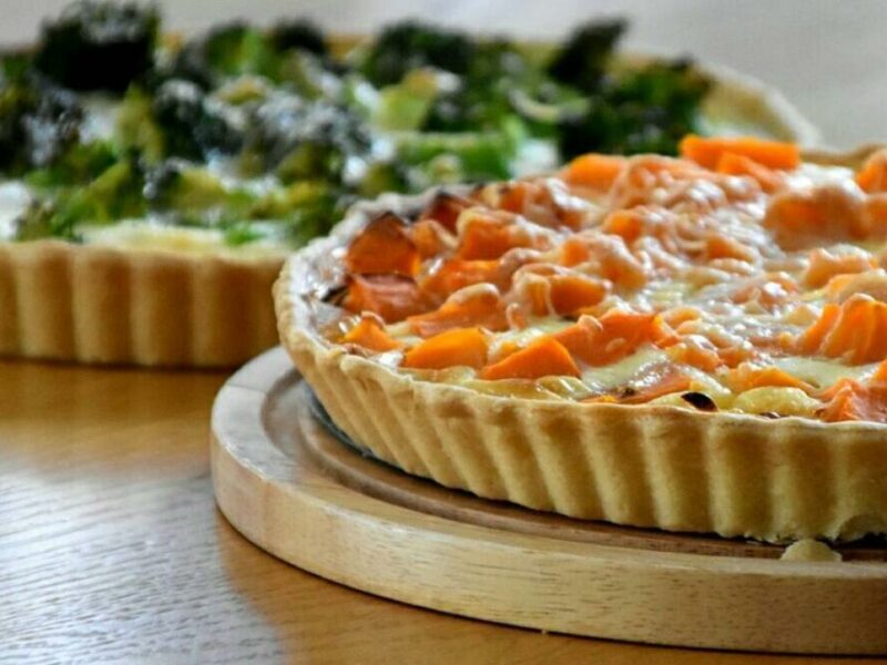 "קיש בטטה וגבינה על קרש עץ; ברקע קיש ברוקולי."