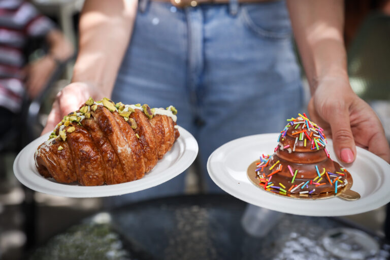 ידיים מחזיקות שתי צלחות, אחת עם קרואסון והשנייה עם קינוח שוקולד